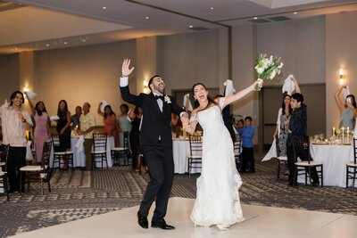 A newlywed couple with their arms out as they celebrate at their reception 