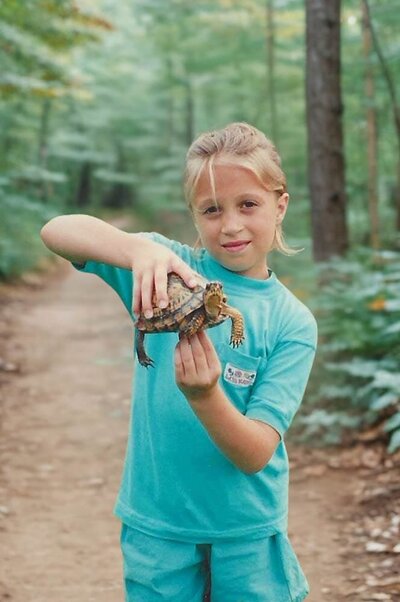 Childhood photo of Stacey Xanthe from Xanthe Bookkeeping standing on a forest trail in Pennsylvania holding a turtle, representing the start of her adventurous spirit.
