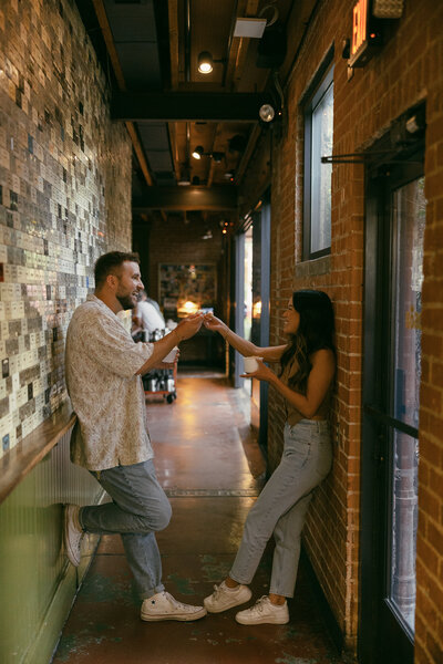 A couple leaning on opposite sides of a hallway reaching out to touch spoons.