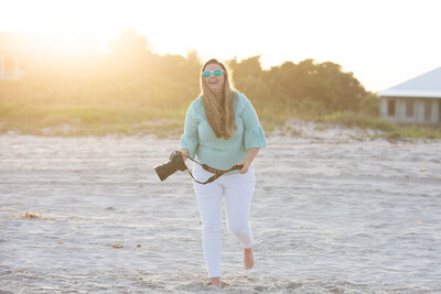 Photographer holding a canon camera walking on the beach smiling with the sun shining at sunset