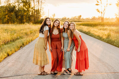 high school friends smiling for a senior photo on a backroad at sunset