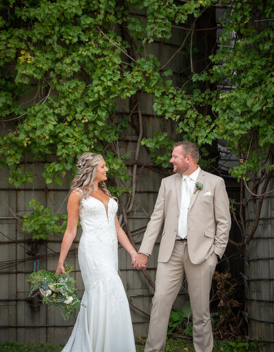 bride and groom hold hands in front of wall with vines