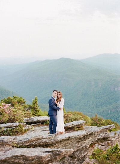 Couple On Rocks with Mountain Background Hugging smiling at Camera Photo