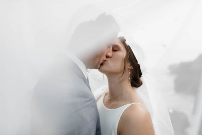 A newlywed couple kissing under a veil 