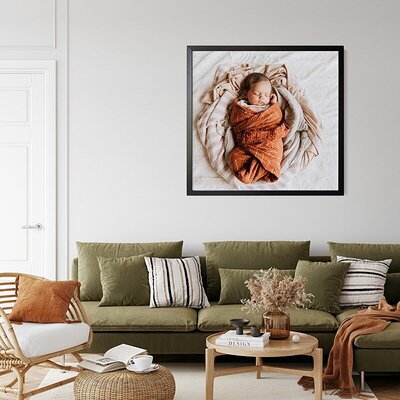 A framed newborn heirloom print hangs above a green couch