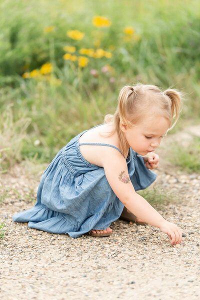 A little girl with blonde pigtails bending down to pick up a pebble