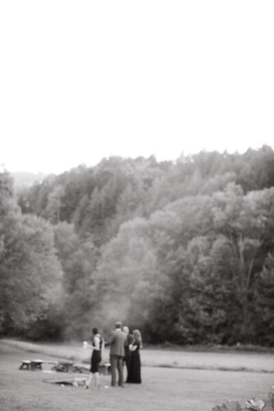 A portrait-style black and white photo shoes a small group of people during an intimate wedding in nature