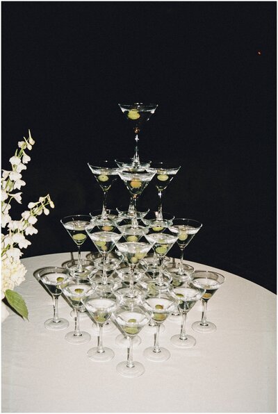 A tower of martini glasses stands on a white table at night