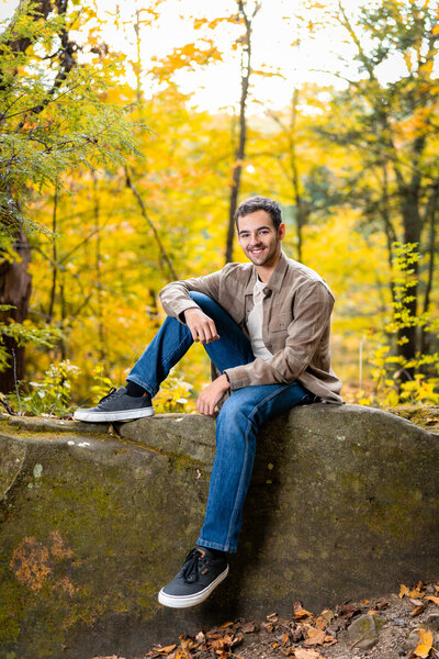 high school senior photography of a senior sitting on a rock in the woods at McConnell's Mill state park near Pittsburgh PA