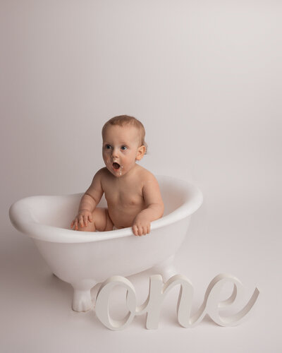 Smiling baby sitting in a small tub with the word one in front