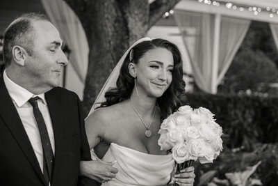 A bride cries happy tears as she walks down the aisle, arm in arm with her father. Her wedding photographer Sarasota captures the moment.