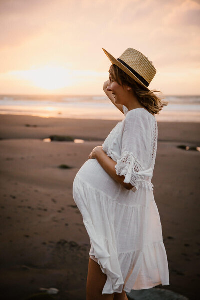 An expectant mother walking along the beach as instructed by her maternity photographer in taranaki