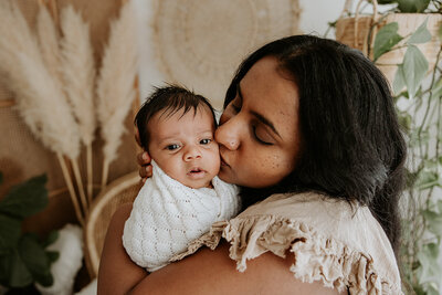 Mother kisses newborn baby at studio newborn session