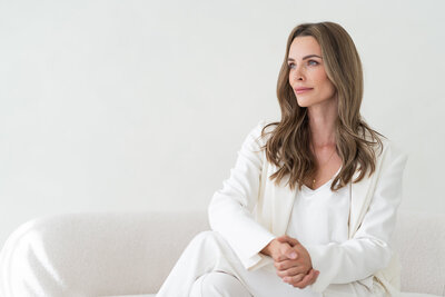 žena v bílém kostýmku sedící na světlé pohovce a dívající se doleva