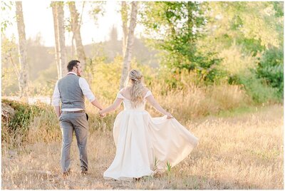 bride and groom walking together away from the camera in the golden sunlight  in a tree lined grassy field