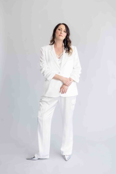 Brand strategist in luxurious white power suit striking confident pose against minimalist grey backdrop during professional brand photoshoot