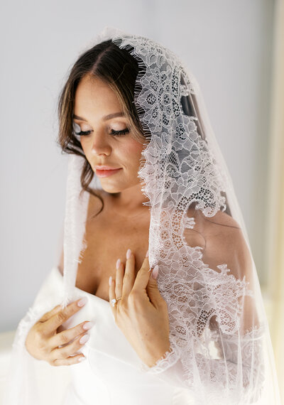 Bridal portrait with veil on bride's head while she soft smiles down at the ground.