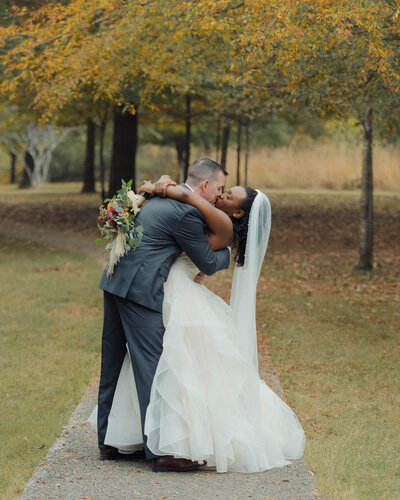 a bride and groom share a dip kiss under some yellow fall foliiage