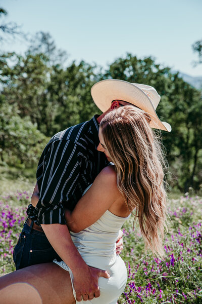 Couple embracing in a field of wildflowers, sharing an intimate moment with the groom wearing a cowboy hat during their elopement