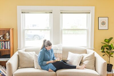 Burgeoning Bud  Post Partum Doula writes in book sitting on couch during Branding photo session with Sara Sniderman Photography in Natick Massachusetts