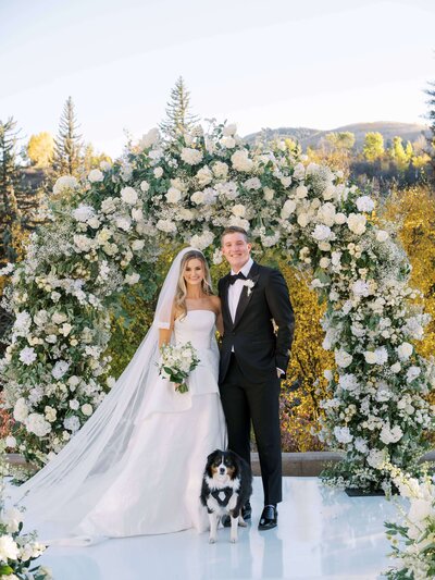 Bride and groom pose with dog, dressed in black tie, at Vail luxury wedding. 