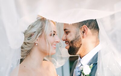 A newlywed couple smiles and looks at each other under the brides veil. taken at stonehouse villa by austin wedding photographer