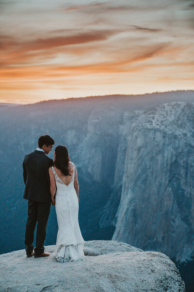Bride and Groom at Taft Point standing on a cliff overlooking Yosemite Valley at sunset by Yosemite elopement photographer Kasey Mantiply