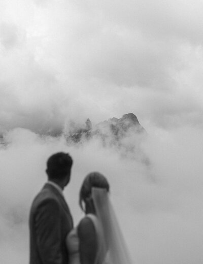 a couple getting married looking at a mountain peak with clouds surrounding it