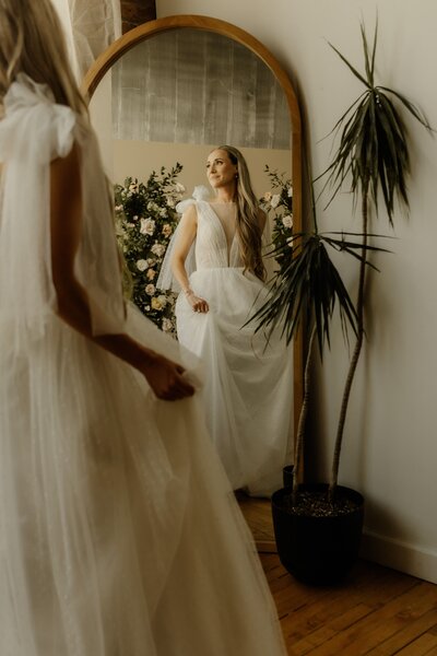 A lovely bride spins in her whimsical wedding dress in front of a mirror.