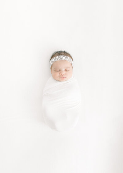 Newborn photo of a baby girl wrapped up laying on a bed in a photo studio Las Vegas