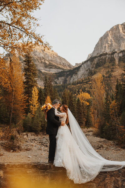 Bride and groom embracing in front of fall foliage and mountain views in Glacier National Park during their elopement.