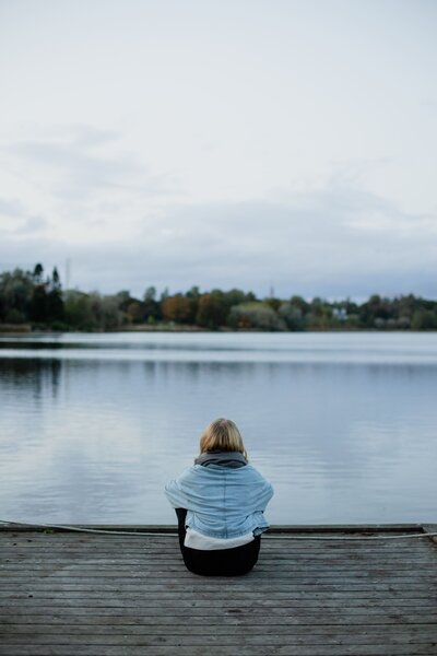 Hyvinvointivalmentaja istumassa rannalla ja katsoo kohti sinistä järveä