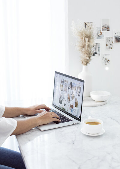 photo of a woman's arms typing on a laptop on a desk next to a cup of tea. 