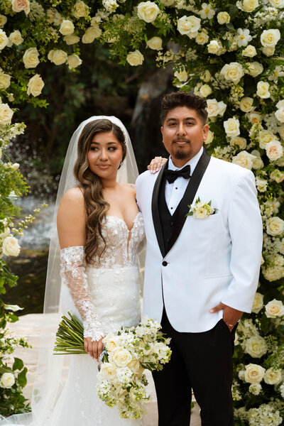 a bride and groom portrait in front of an arch of white flowers