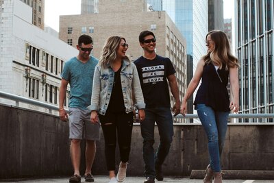4 teens walking, white male and female, cityscape in background