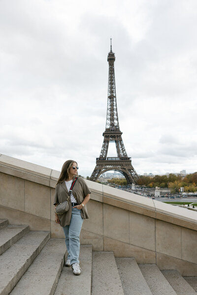 Destination Elopement Photographer Gaby standing on the Trocadéro steps in Paris with the Eiffel Tower in the background, capturing the essence of travel and adventure.