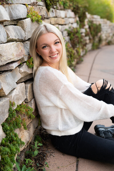 High school girl sits and leans against a rock wall for her senior pictures at Centennial Lakes Park in Edina, Minnesota.