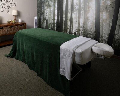Massage bed draped in a green blanket in front of a full wall mural of nature