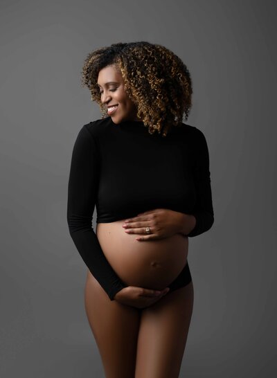 Pregnant women in black crop top smiling and holding her baby bump. Photo taken at Atlanta Maternity photo studio in Woodstock GA.