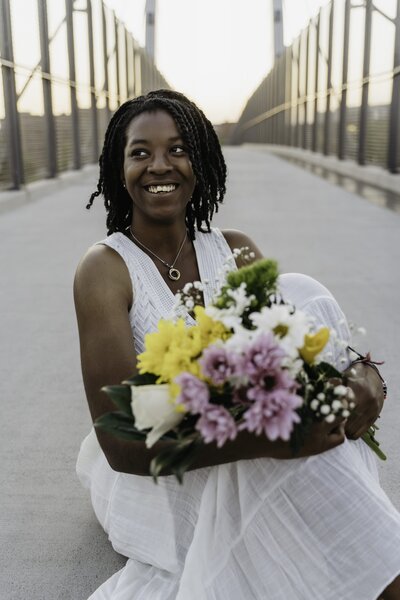 Senior girl sitting on a bridge holding flowers during a session with Sophie Grace Photography