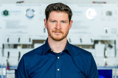 Professional headshot of man in blue shirt smiling confidently against neutral gray studio background new jersey.