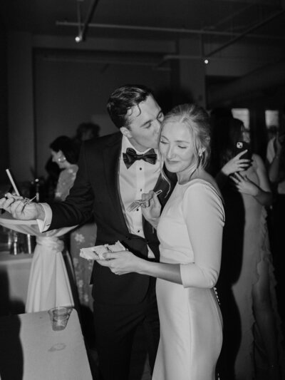 Groom Kisses Bride On The Cheek While Cutting The Cake