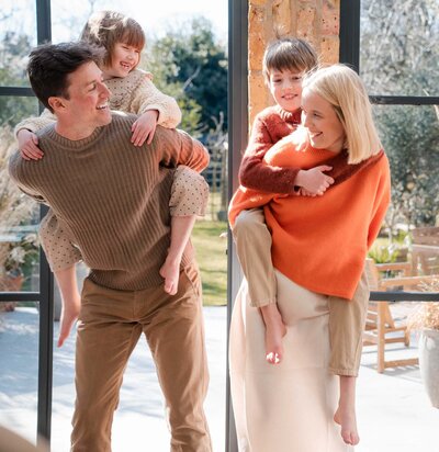 Four people pose together indoors by large windows in casual autumn-toned sweaters and clothing.