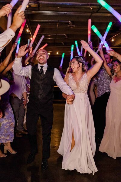 Bride and groom cheering loudly with big smiles on their faces as they go through light stick tunnel exit after wedding dancing