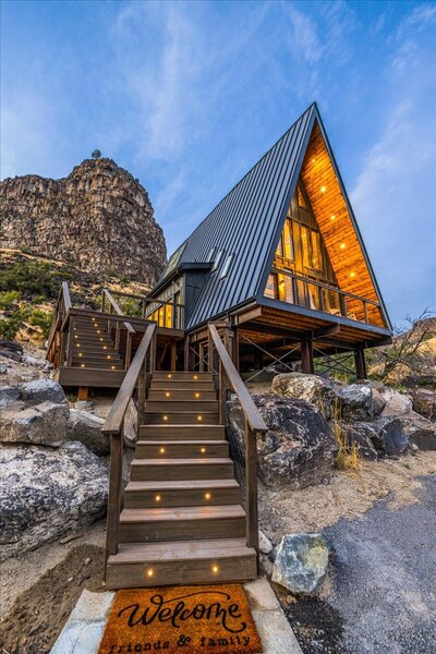 The nearly completed Perrine Hideaway A-frame cabin, featuring a black metal roof, large glass windows, and a rugged canyon backdrop