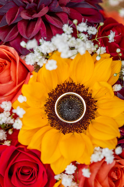 Detail wedding photo in Boone, NC of a wedding band sitting on a sunflower in a bridal bouquet.