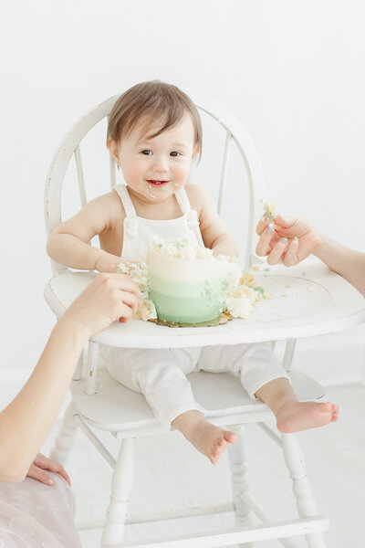 One year old baby boy smiles while smashing his birthday cake during portrait session