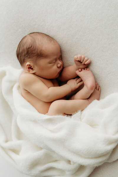 A newborn baby lies sleeping in the fetal position, wrapped in soft blankets inside a vancouver Washington natural light studio.