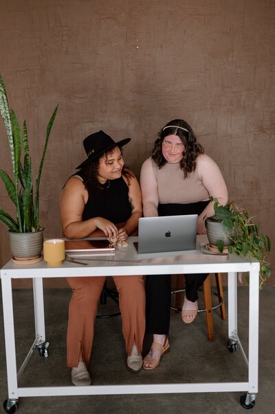 Ashley and Katelin sitting at a table working on a details for a wedding.