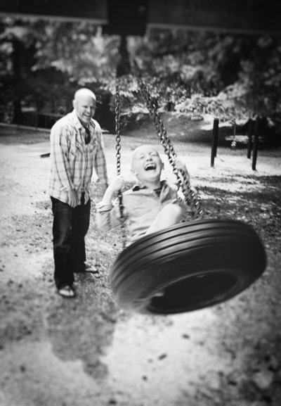 black and white photograph of a dad pushing a laughing child on a tire swing by Spearfish, South Dakota photographer Rooted and Wild Photography